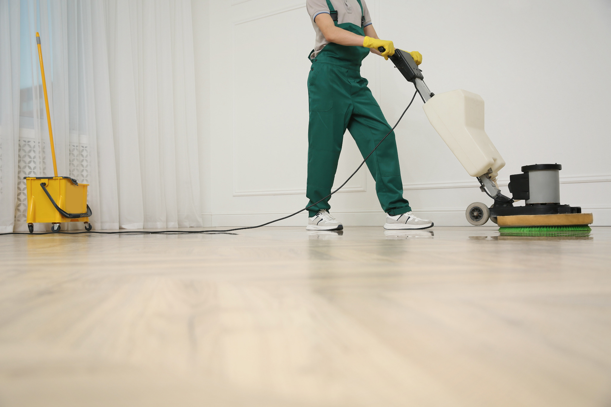 School Floor Buffing in Clapham on a light oak plank hardwood classroom floor, technician using a rotary buffer beside a yellow mop bucket.