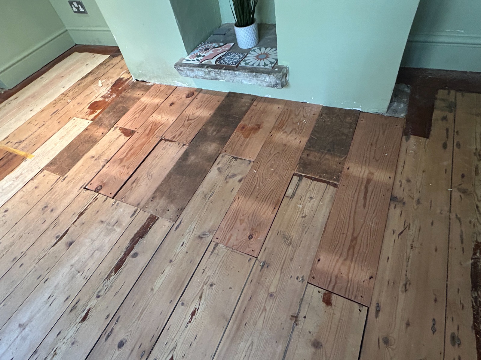 Clapham Floor Sanding repairs on Victorian pine floorboards in a Clapham living room, showing mixed replacement softwood boards around the fireplace before full sanding and finishing.