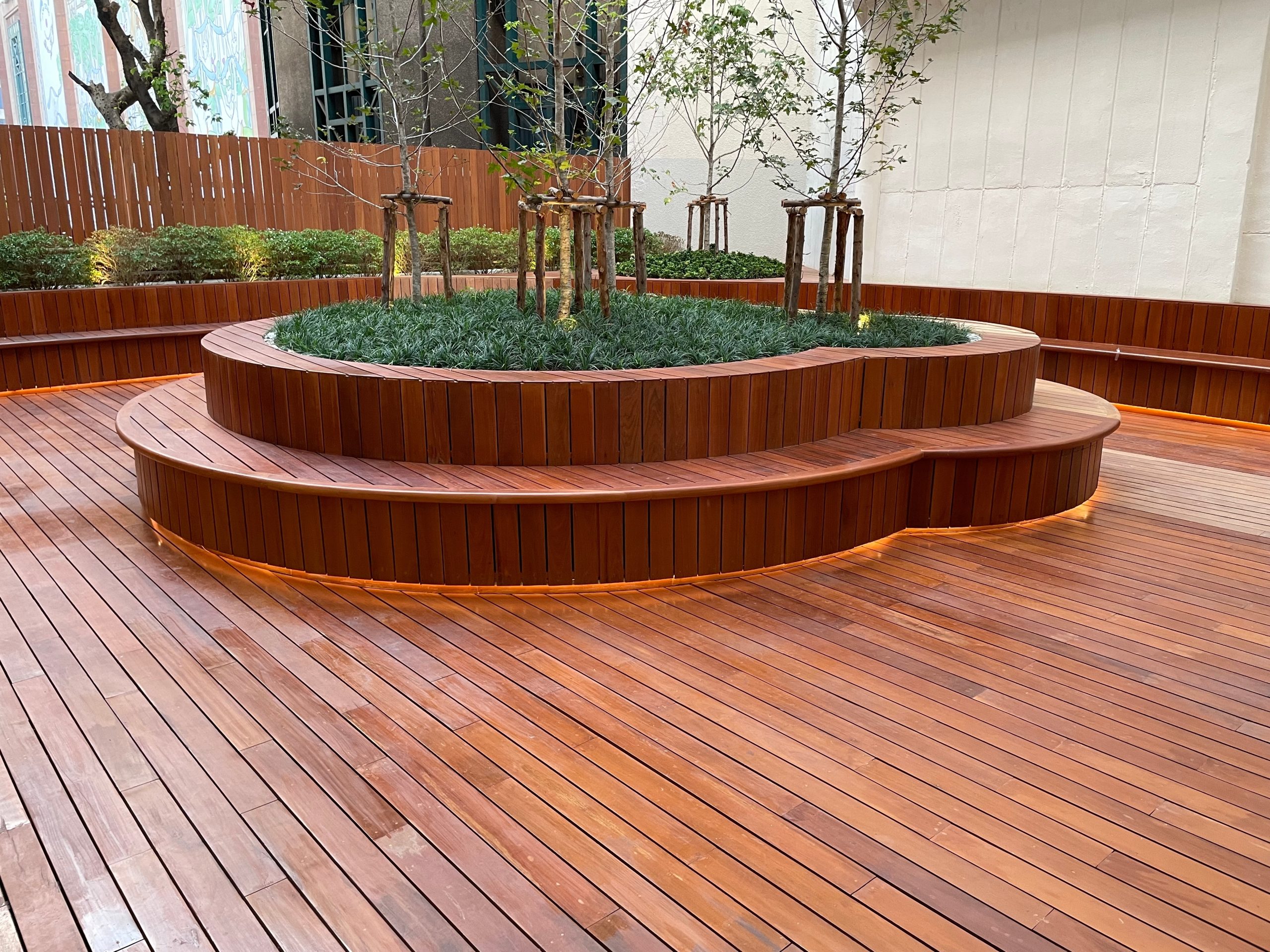 Deck Sanding and Renewal in Clapham on a hardwood timber courtyard deck floor, showing smooth, rich-coloured boards around curved raised seating and planting.