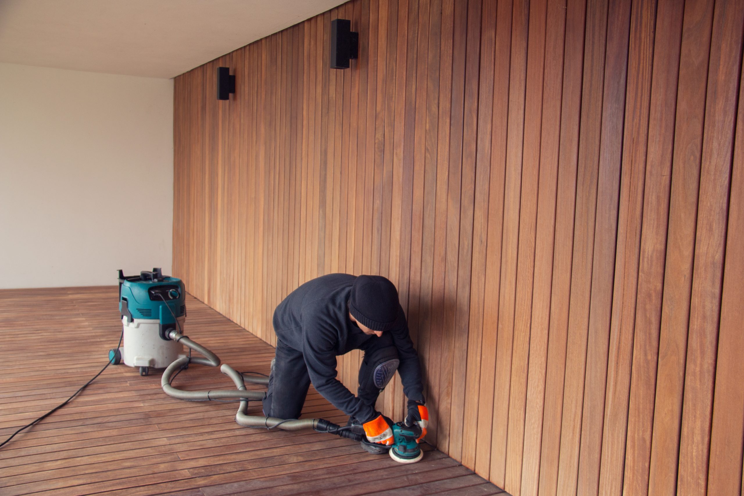 Deck Sanding and Renewal in Clapham on a hardwood timber deck floor, with a professional sanding the boards along a matching timber wall for a smooth, safe finish.