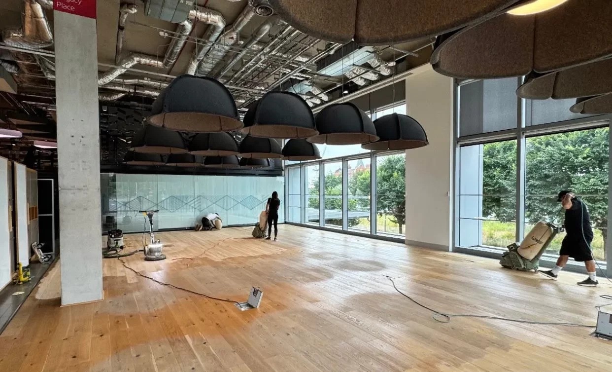 Deck Sanding and Renewal in Clapham carried out on an oak wide-plank hardwood floor in a modern commercial space, with technicians sanding the large timber surface.