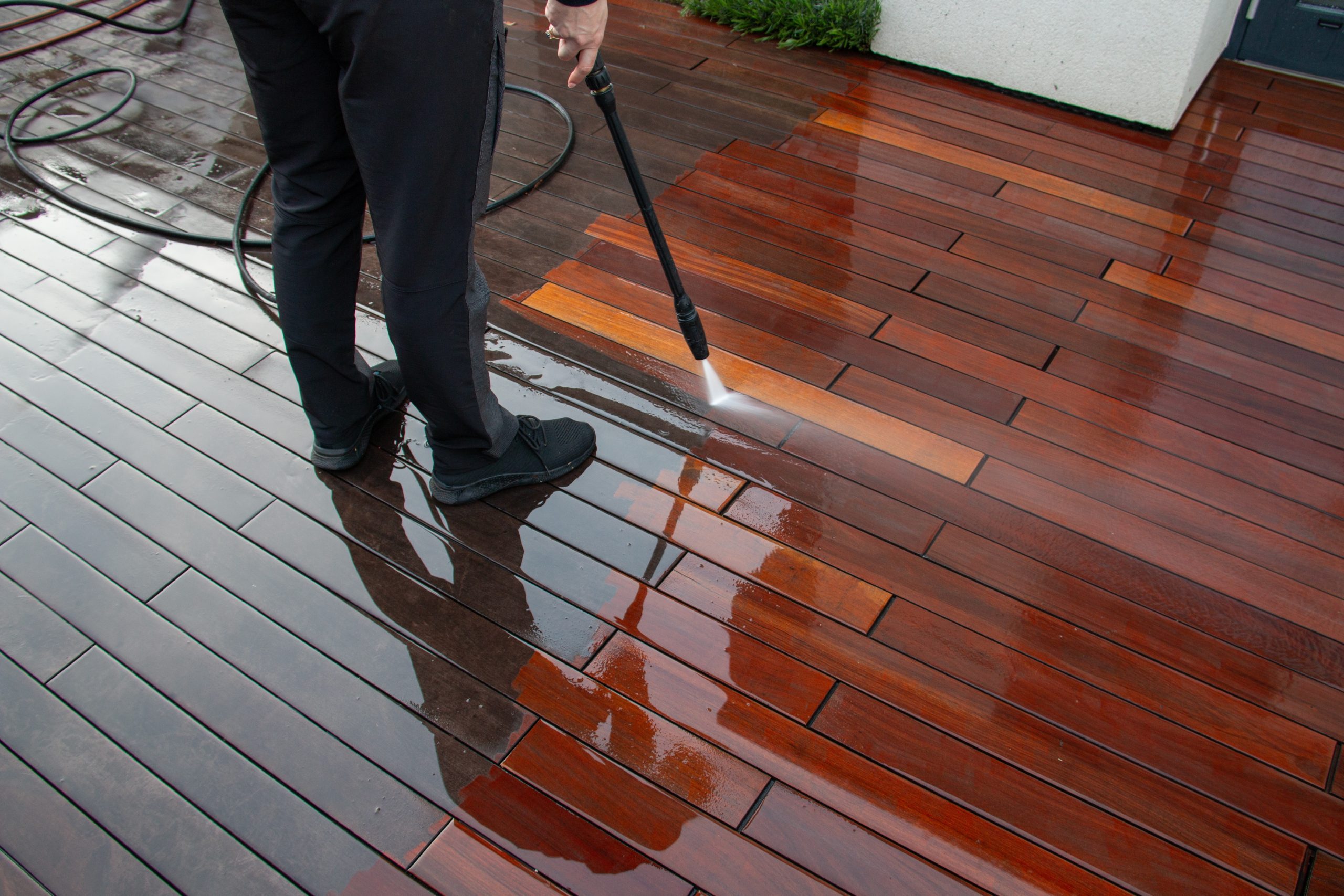 Deck Sanding and Renewal in Clapham on a polished hardwood timber deck floor, with a professional jet-washing the rich brown boards after restoration.