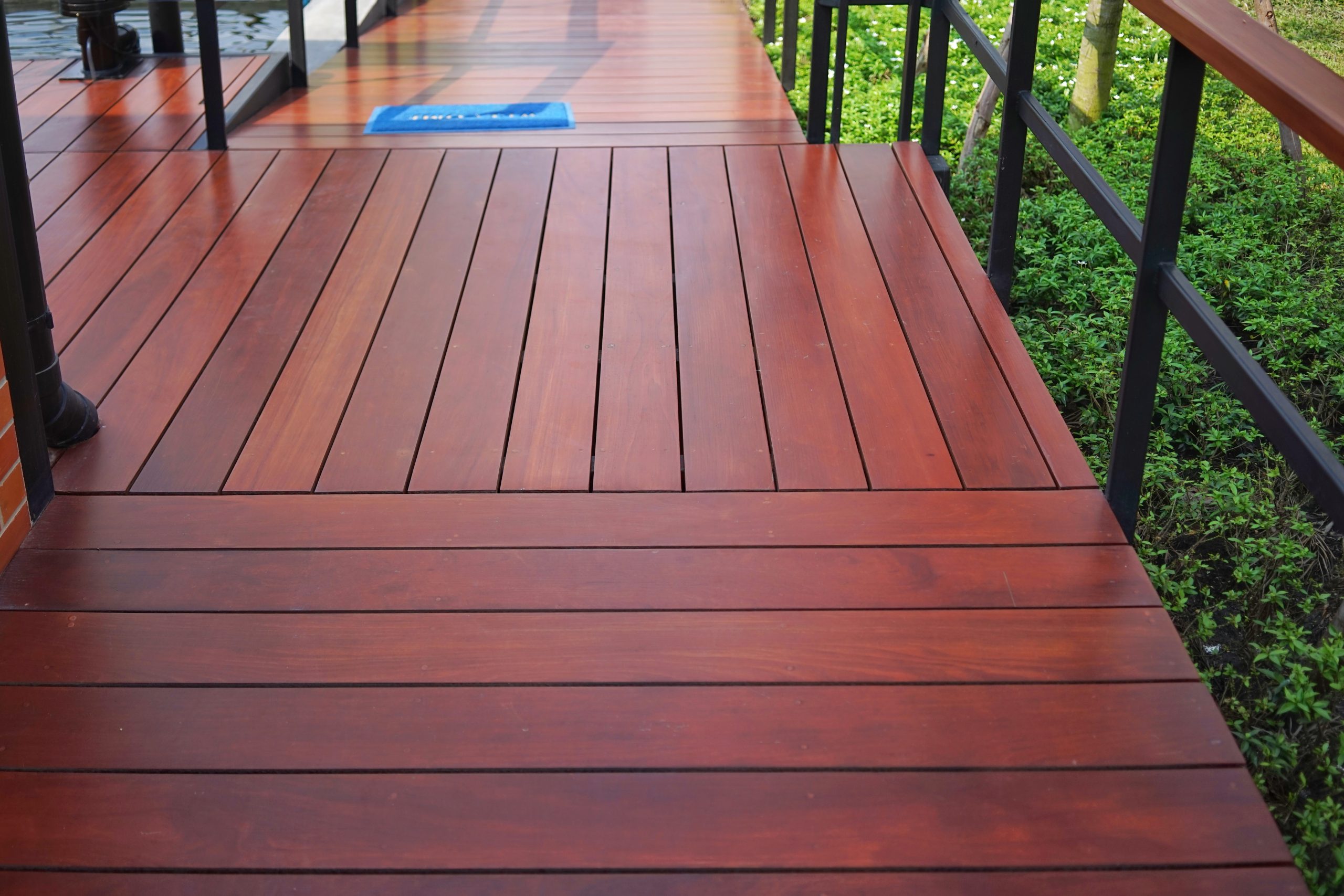 Deck Sanding and Renewal in Clapham on a smooth hardwood timber garden deck walkway, showing rich red-brown boards beside metal railings and greenery.
