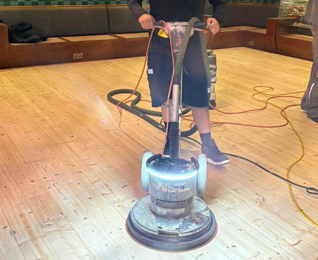Wood Floor Sanding in Clapham commercial venue, with a technician buffing a softwood pine floor using a rotary machine to smooth and prepare the sanded boards for finishing.