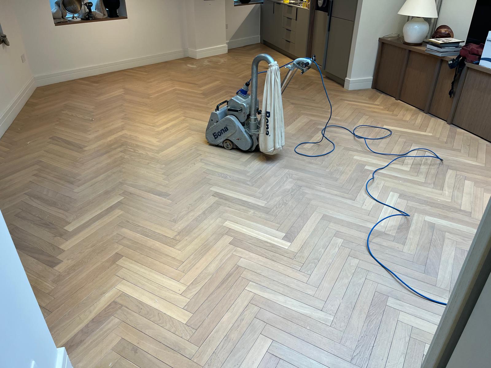 Wood Floor Sanding in Clapham living room with a light oak herringbone parquet floor being professionally sanded using a Bona dust-extracting machine to prepare the parquet for refinishing.