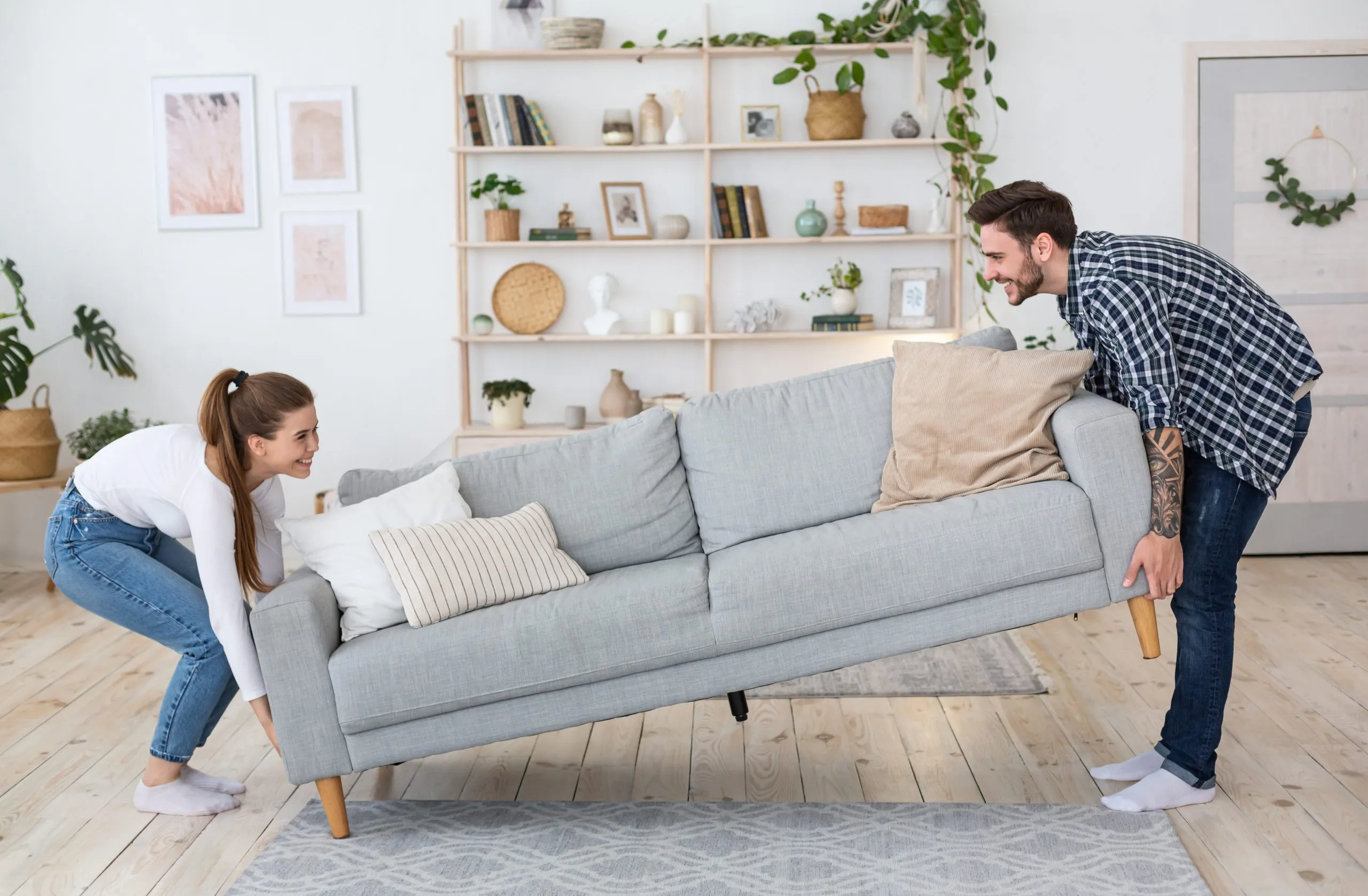 Happy couple moving a sofa in a bright living room after Wood Floor Sanding in Clapham, showing smooth light pine softwood floorboards that have been freshly restored.