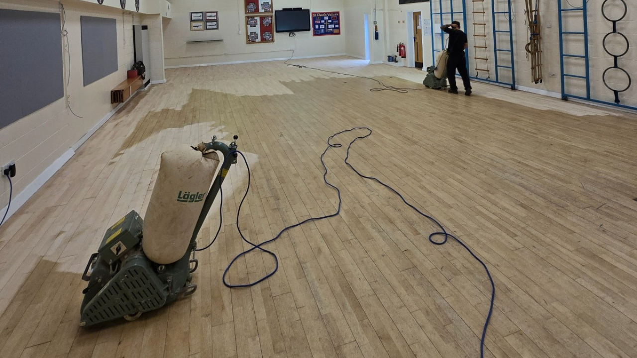 Wood Floor Sanding in Clapham school hall, showing a large maple strip hardwood floor being sanded with commercial dust-extracting machines to refresh the worn surface.