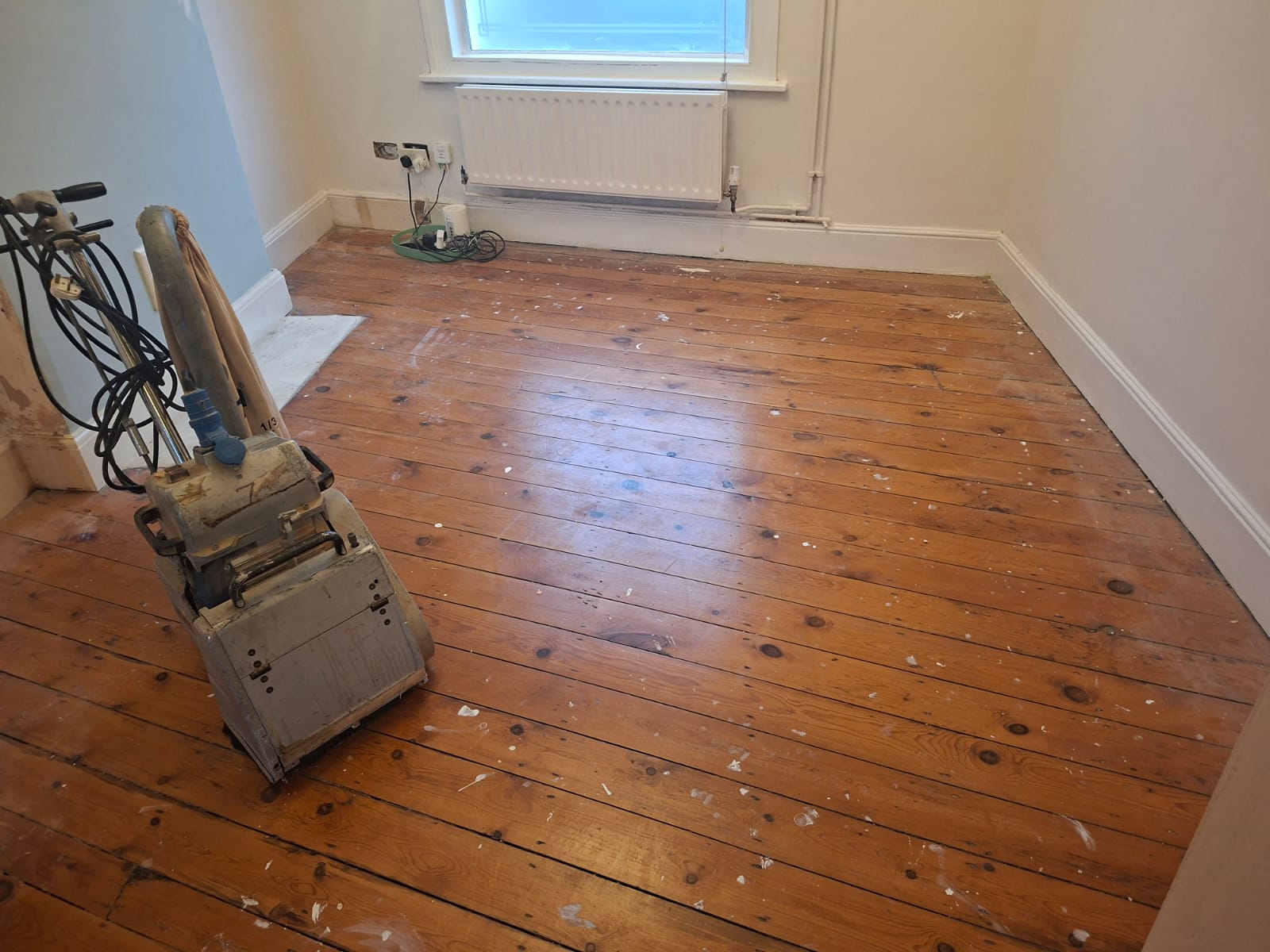 Wood Floor Sanding in Clapham bedroom with original pine floorboards, showing a sanding machine ready to restore the worn, stained timber surface before refinishing.