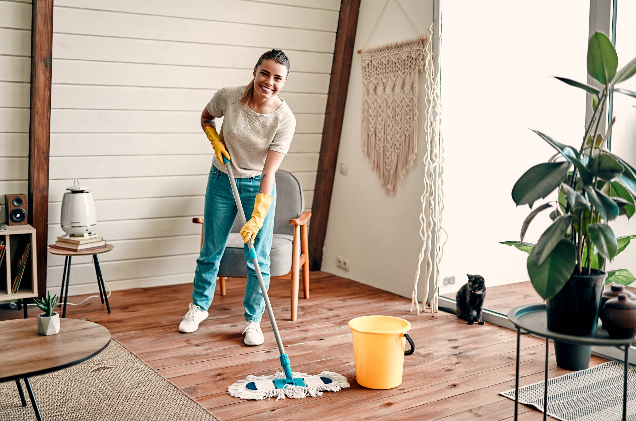 Smiling woman mopping a freshly restored pine softwood living room floor after Wood Floor Sanding in Clapham, showing how easy the smooth timber boards are to keep clean.