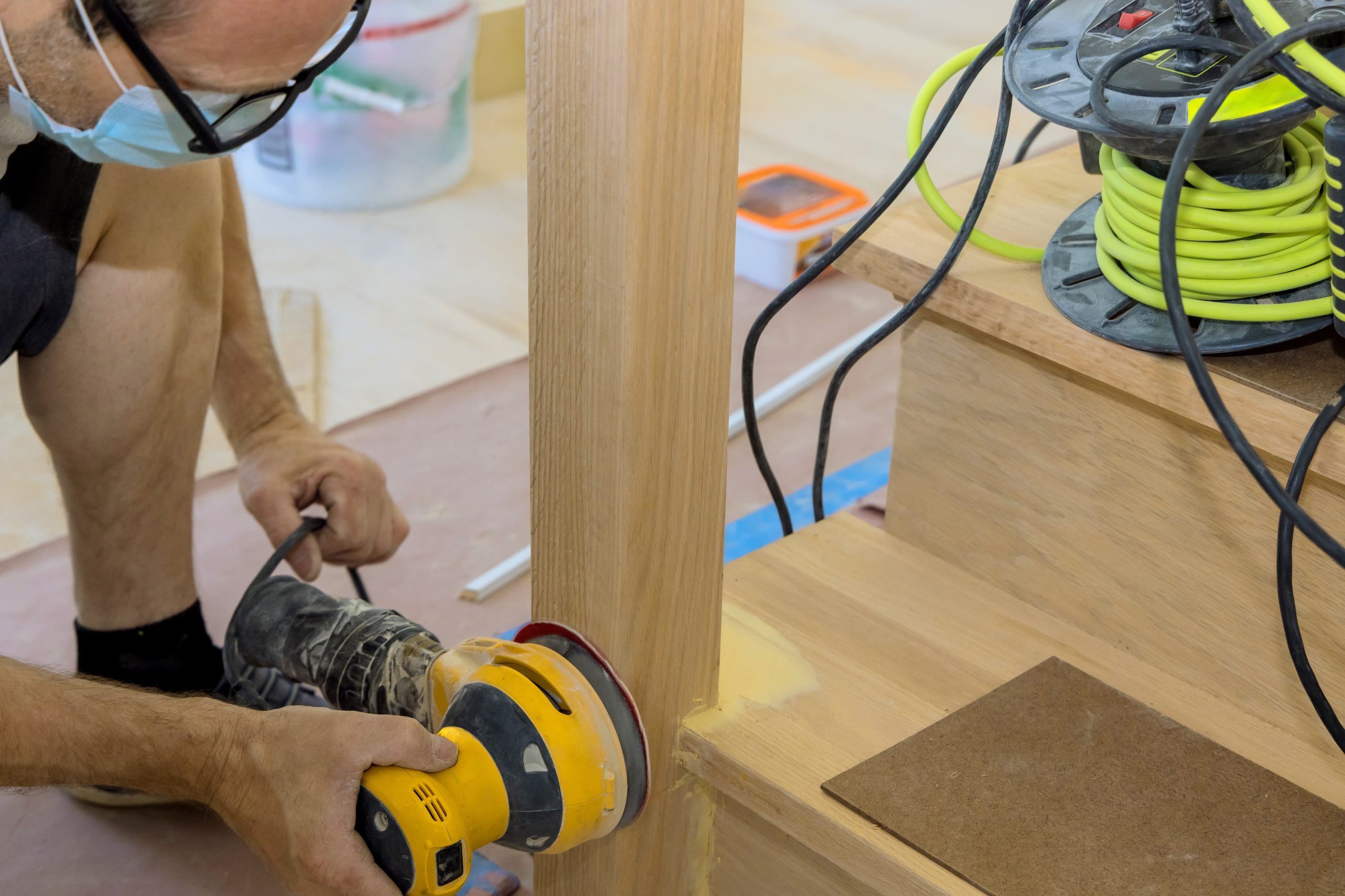 Wood Floor Sanding in Clapham with a technician carefully sanding a solid oak staircase and newel post, preparing the hardwood steps for a smooth, refined finish.